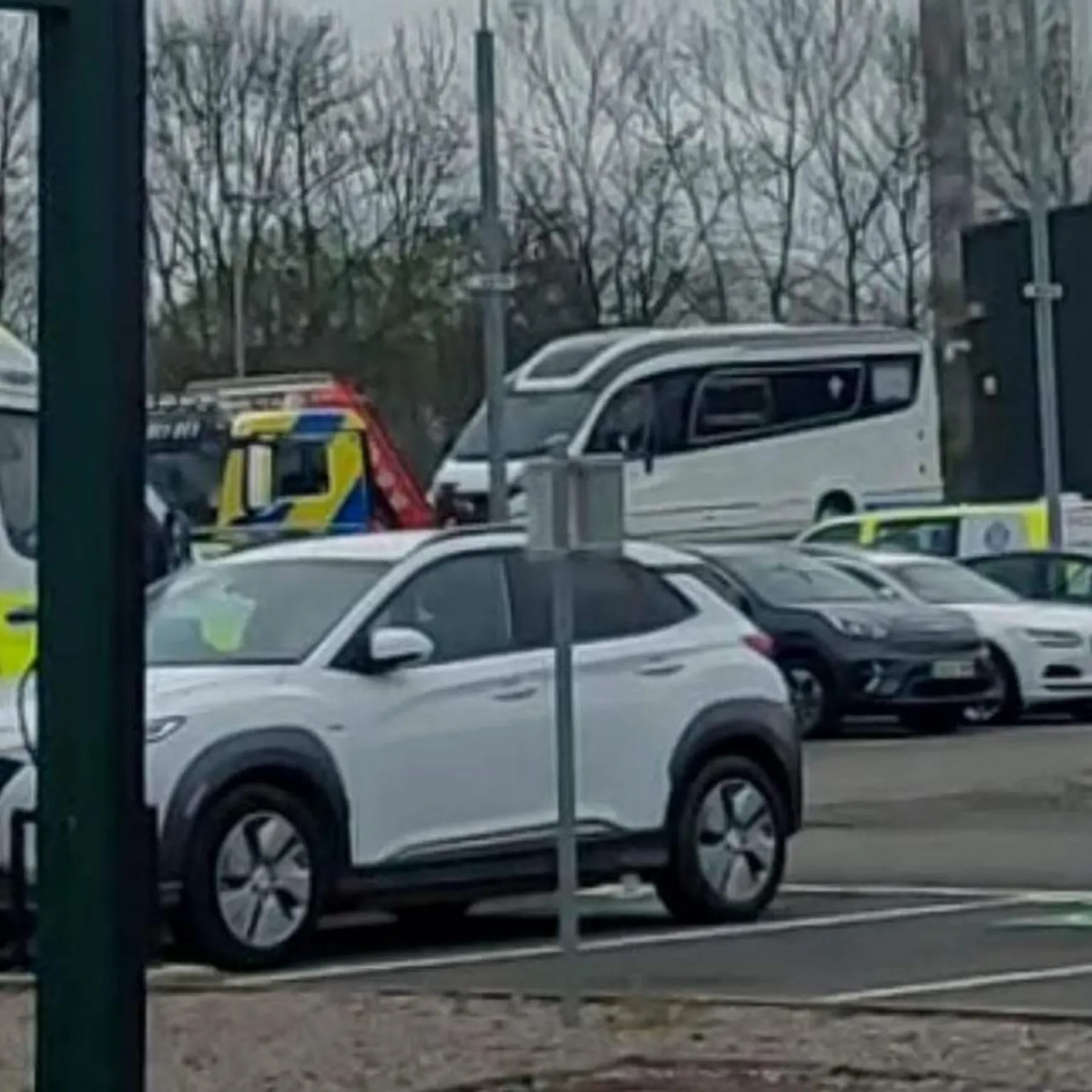 David Cardwell A white campervan in a compound. There us a white car in the foreground and other cars and police vehicles parked elsewhere.