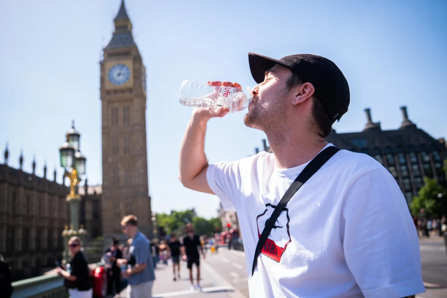  A man in a white t-shirt and black cap cools down with a bottle of water during the hot weather in Westminster Bridge, central London. 