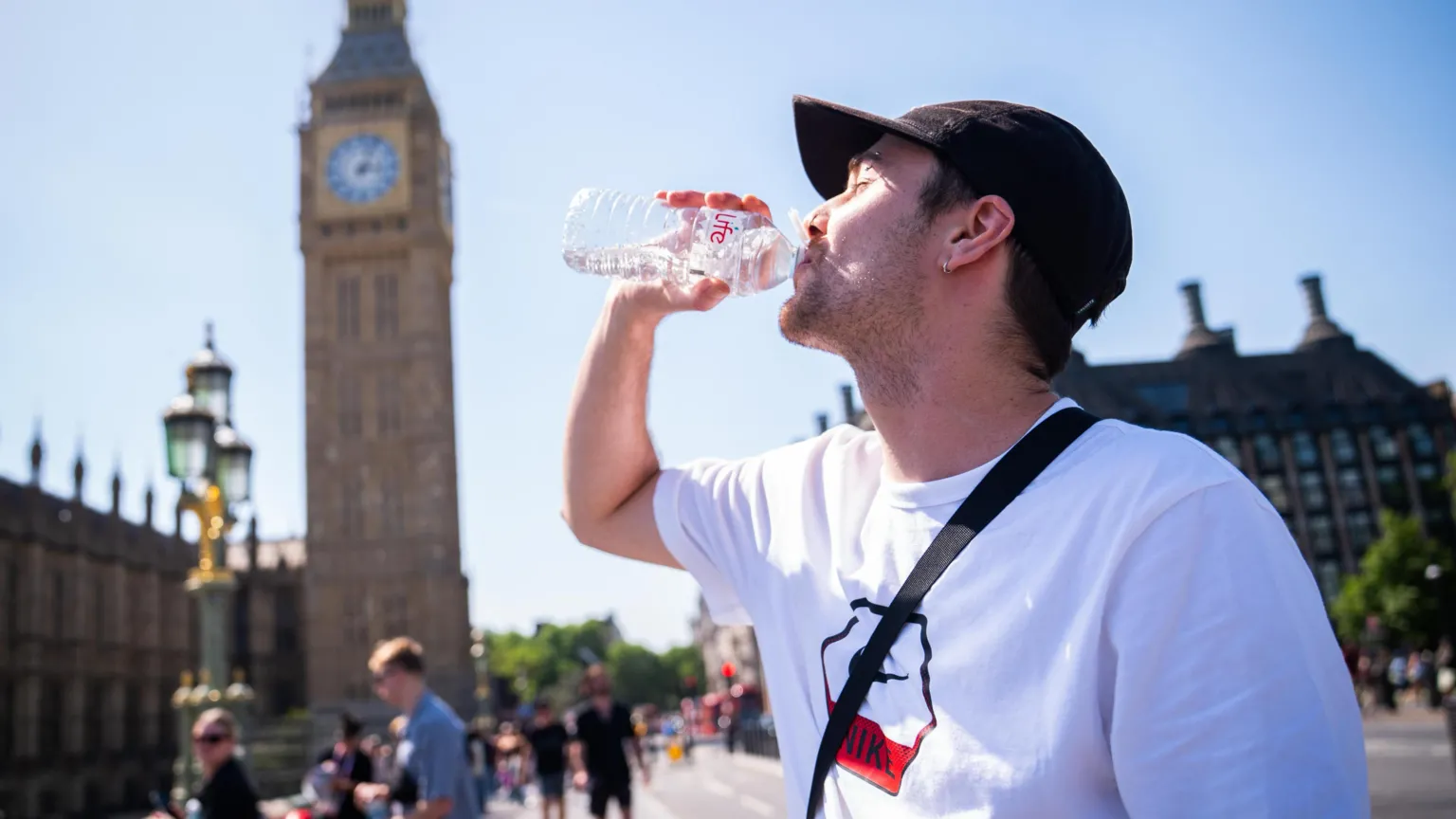  A man in a white t-shirt and black cap cools down with a bottle of water during the hot weather in Westminster Bridge, central London. 