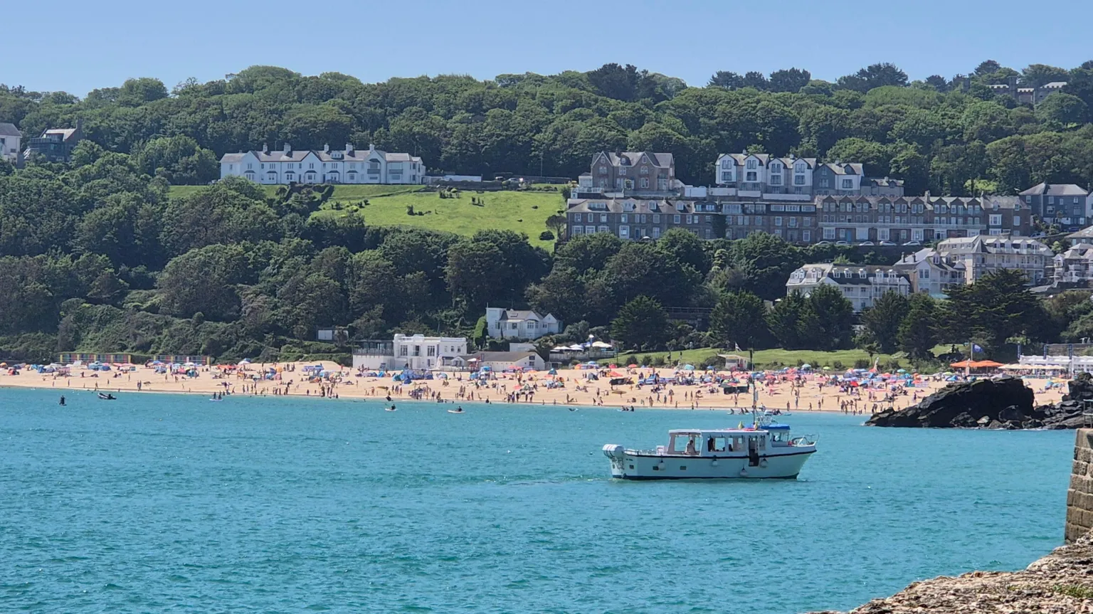 Raven, BBC Weather Watchers A view of a busy beach in St Ives, Cornwall, the sea is crystal blue and a white boat is sailing close to the shore.