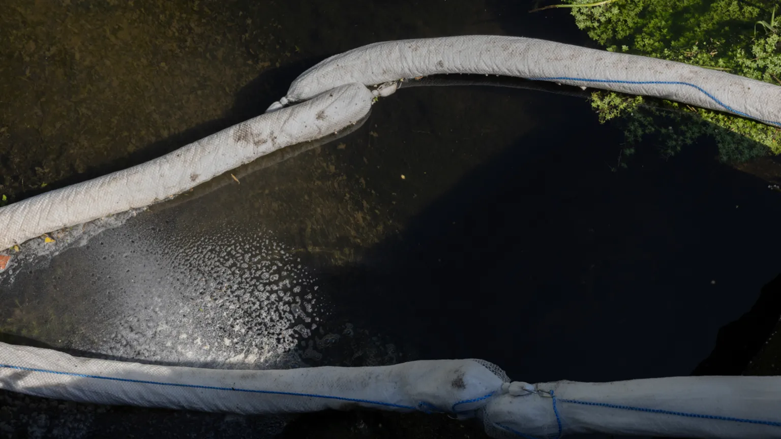 Facundo Arrizabalaga Long white sock-like containment booms hold paler water to the rest of the river.