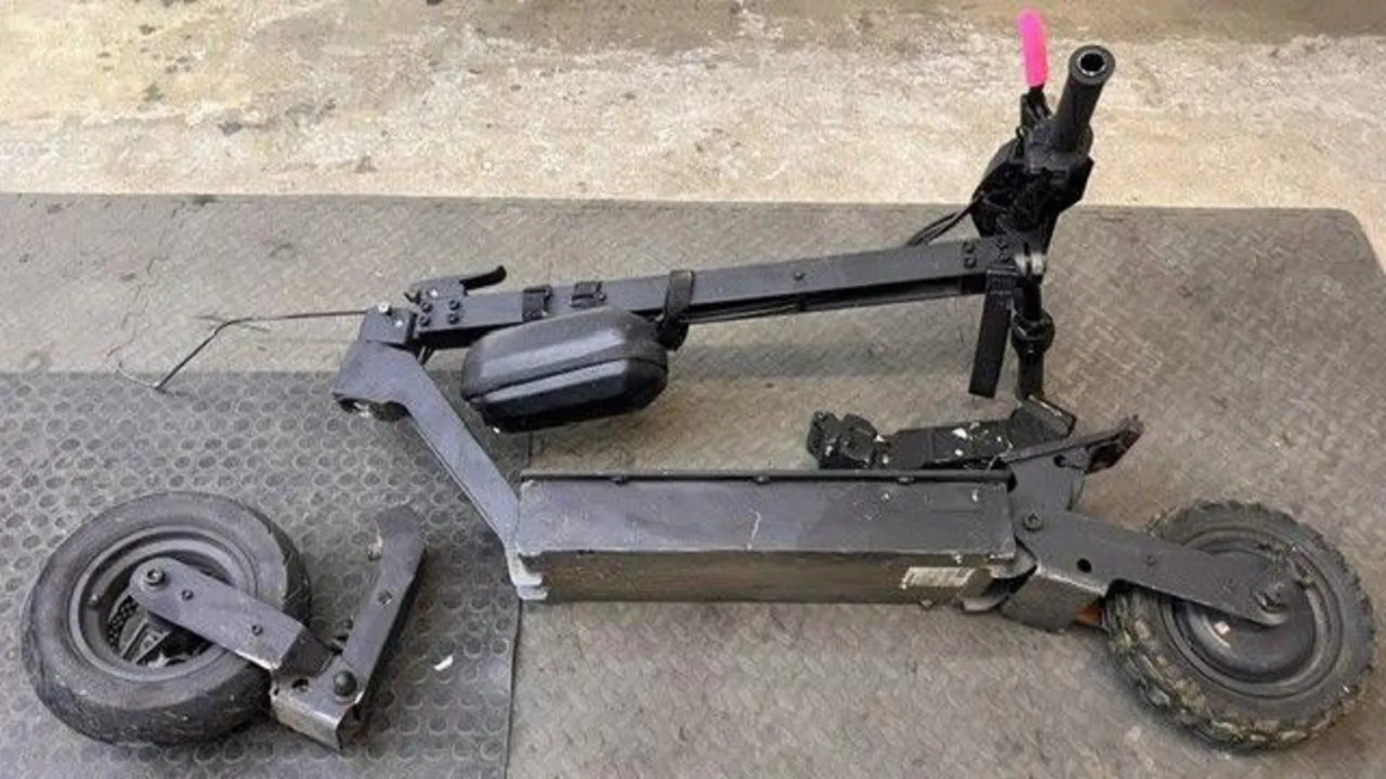 Broken e-scooter pictured on the floor of a repair shop in Aberdeen. The scooter is black with one pink handle. The back wheel and connecting fitting is broken and completely detached from the body of the scooter