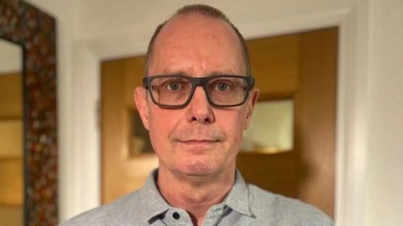 Head and shoulders image of John Neil. He has very short dark hair and dark rimmed glasses. He's looking straight at the camera and is wearing a light grey polo shirt. 