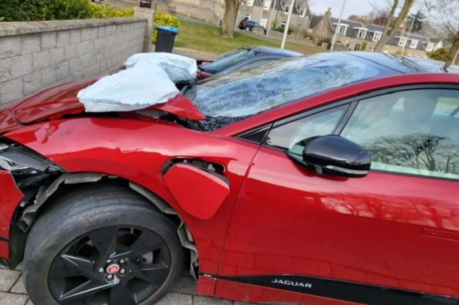 Image of damaged car after e-bike crash. The crash is a bright red Jaguar. The image shows the bonnet and side around the front passenger wheel which are buckled. The front windscreen is also smashed.