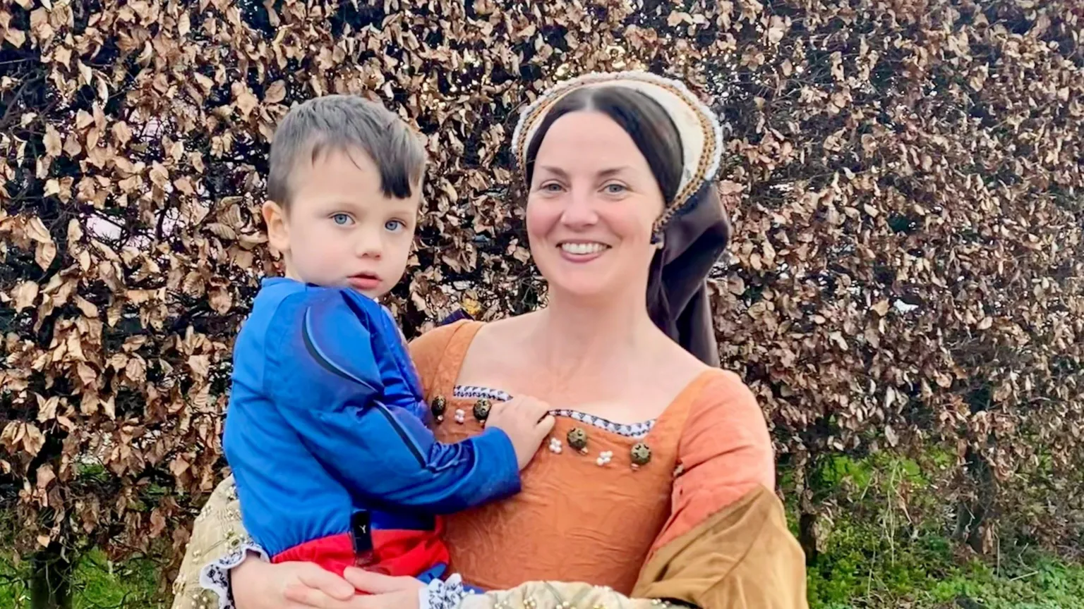 Supplied Hollie dressed in a medieval costume as she holds her son Max in her arms. Max is also wearing a costume, with a blue long-sleeved top and red belt.