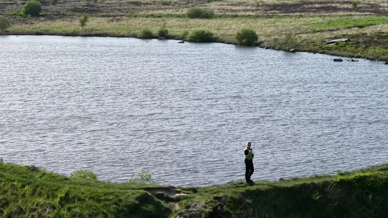 YappApp Police officer stands by a reservoir with a high vis jacket on and dark trousers.