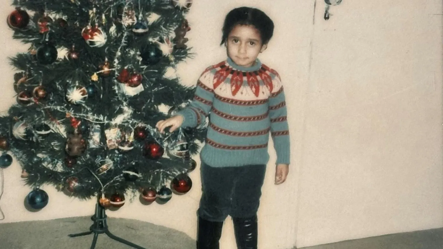 Metropolitan Police A polaroid image of a Andrea Bernard standing next to a decorated Christmas tree. She is wearing a patterned blue, white, and red knit jumper, dark trousers, and black boots.