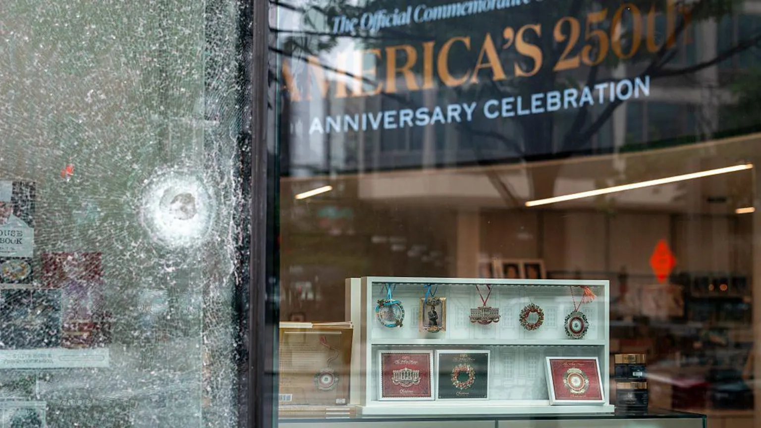 A bullet hole can be seen in the fractured glass window of the White History shop after yesterday's shooting near the White House. Through an intact window pane, one can see a sign declaring,