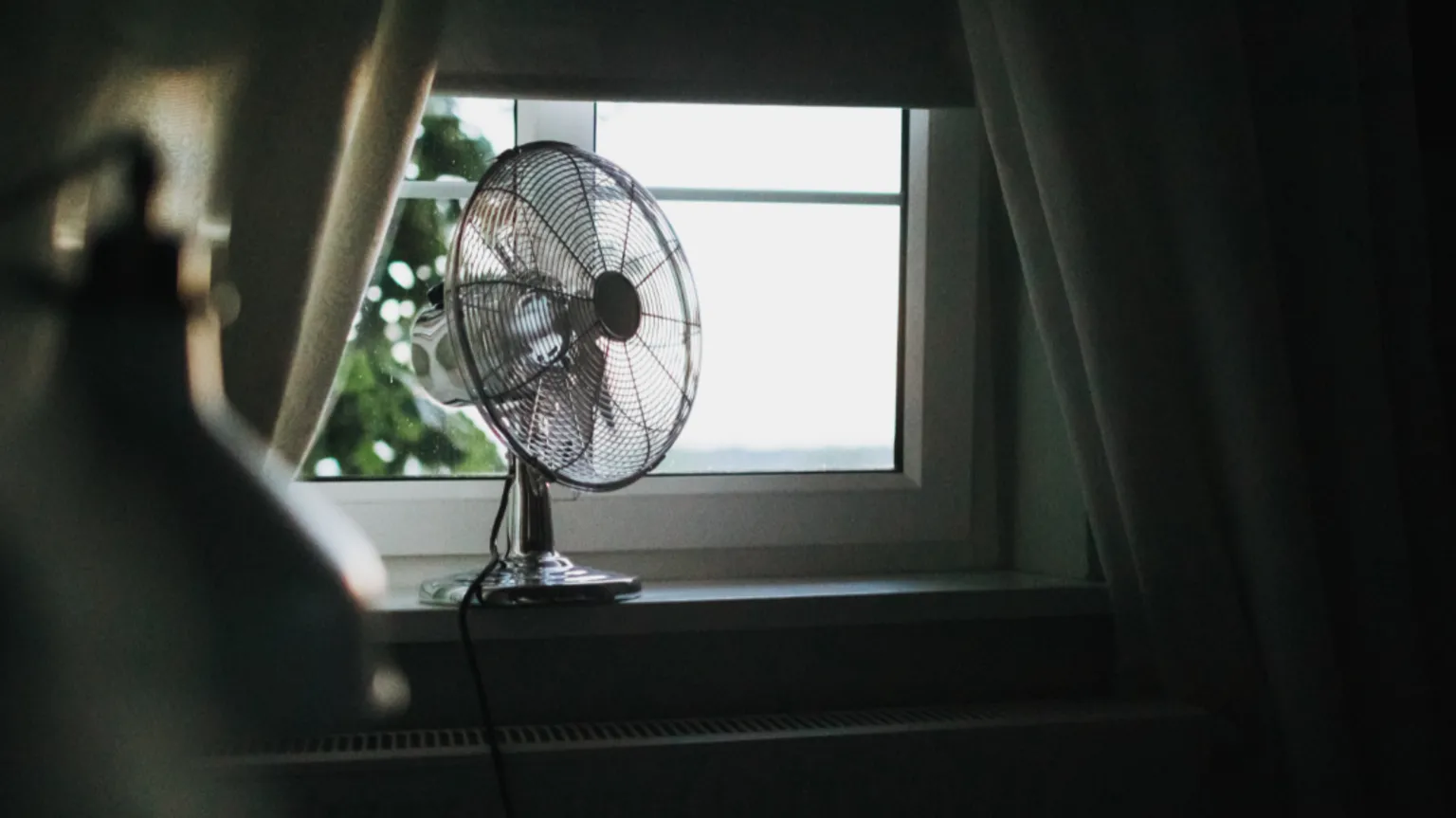  A silver fan is sitting on a bedroom windowsill. 