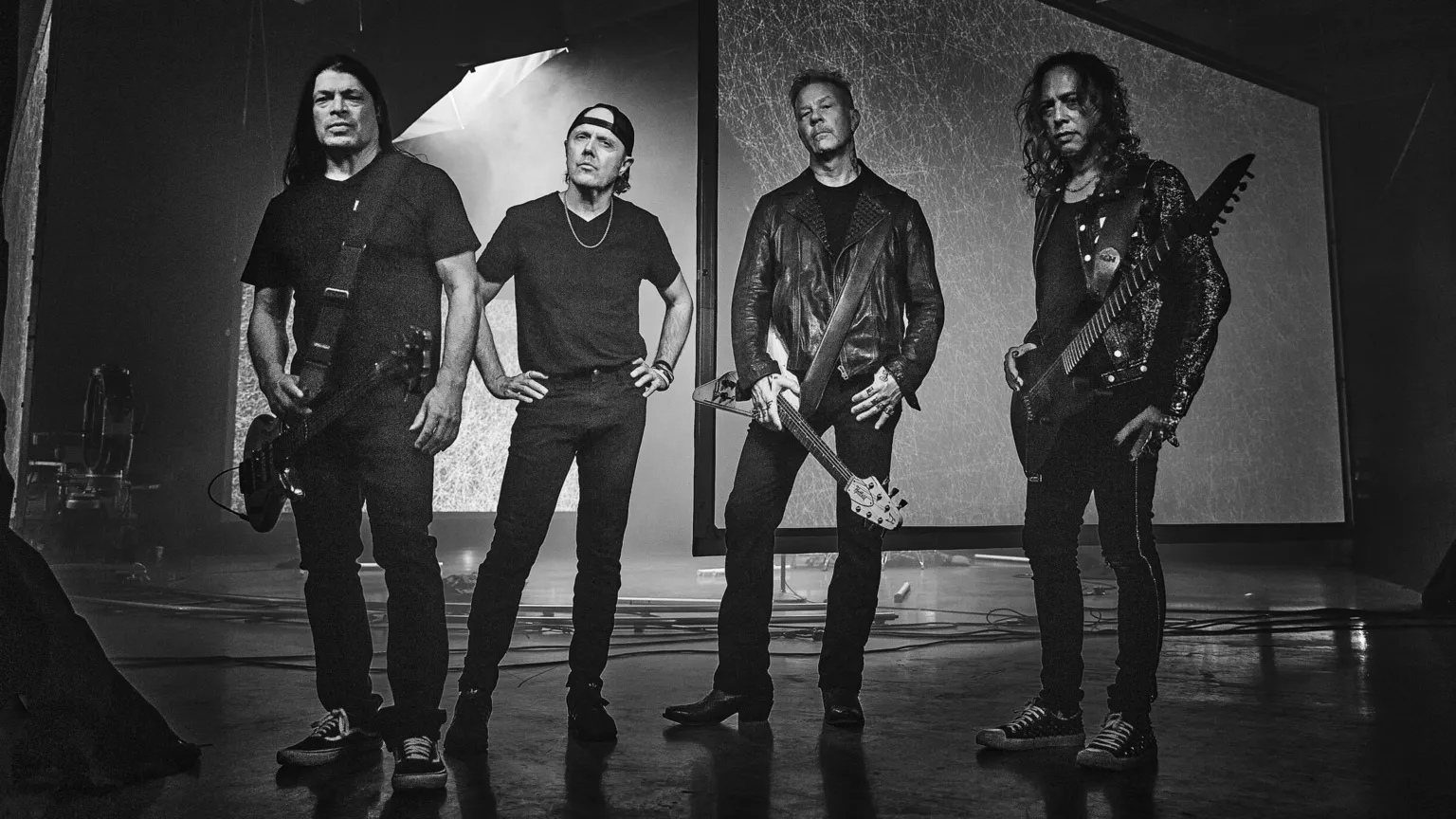 Tim Saccenti Heavy metal band Metallica: four middle-aged men dressed in dark jeans and tops, the two men on either end hold guitars, one man in the middle stands with his hands on his hips and the other holds a guitar.