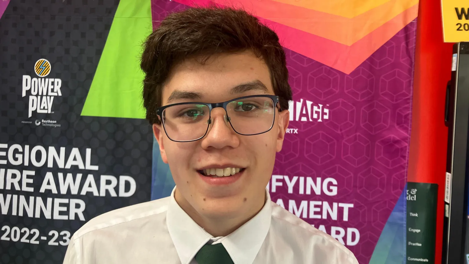 Jonathan smiling at the camera. He is wearing glasses, a white shirt and green tie. He has dark brown hair.