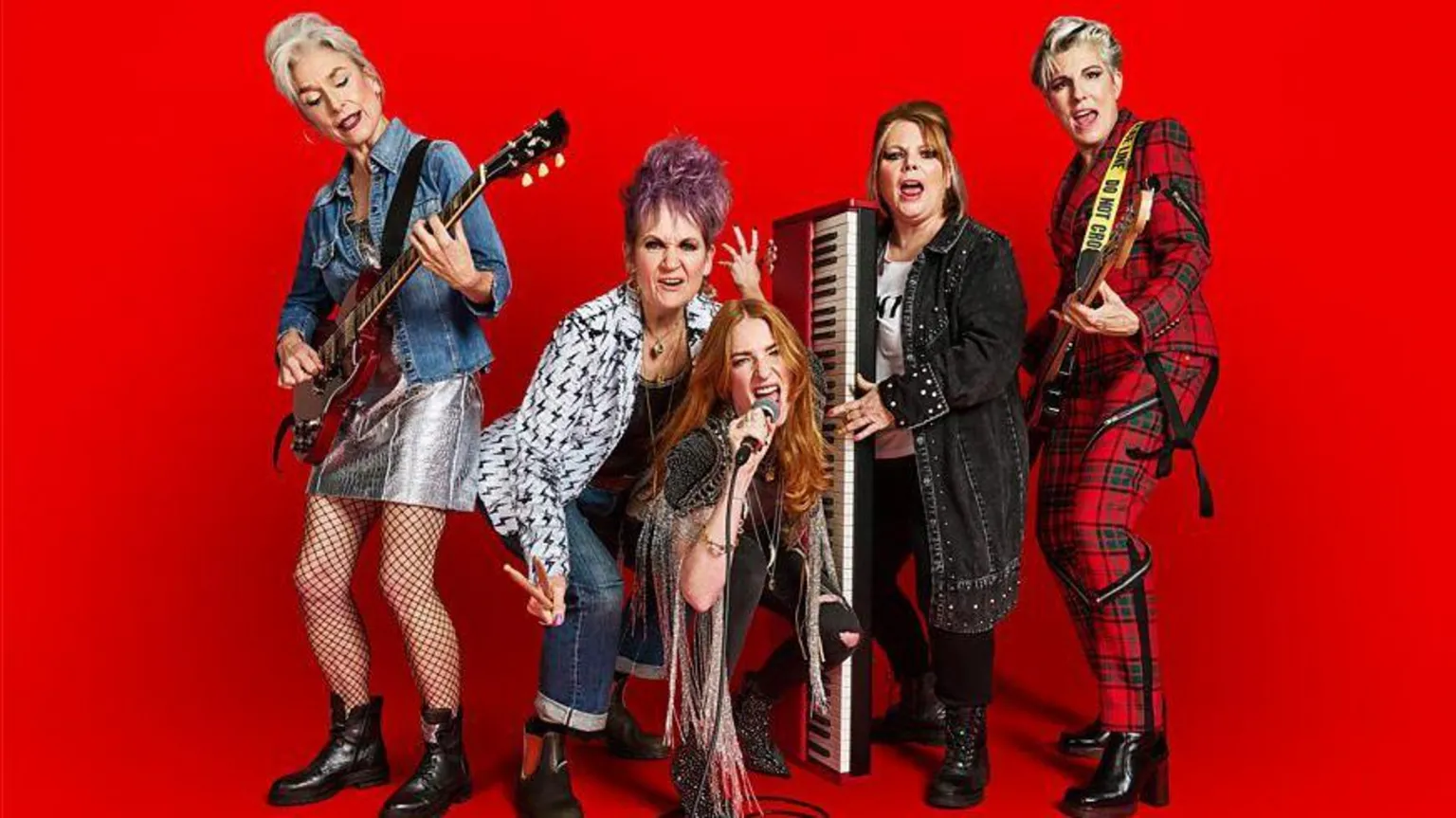 BBC/Drama Republic/Julia Kennedy Five middle aged women wearing punk rock outfits, eahc holding a different musical instruments and standing against a red background.