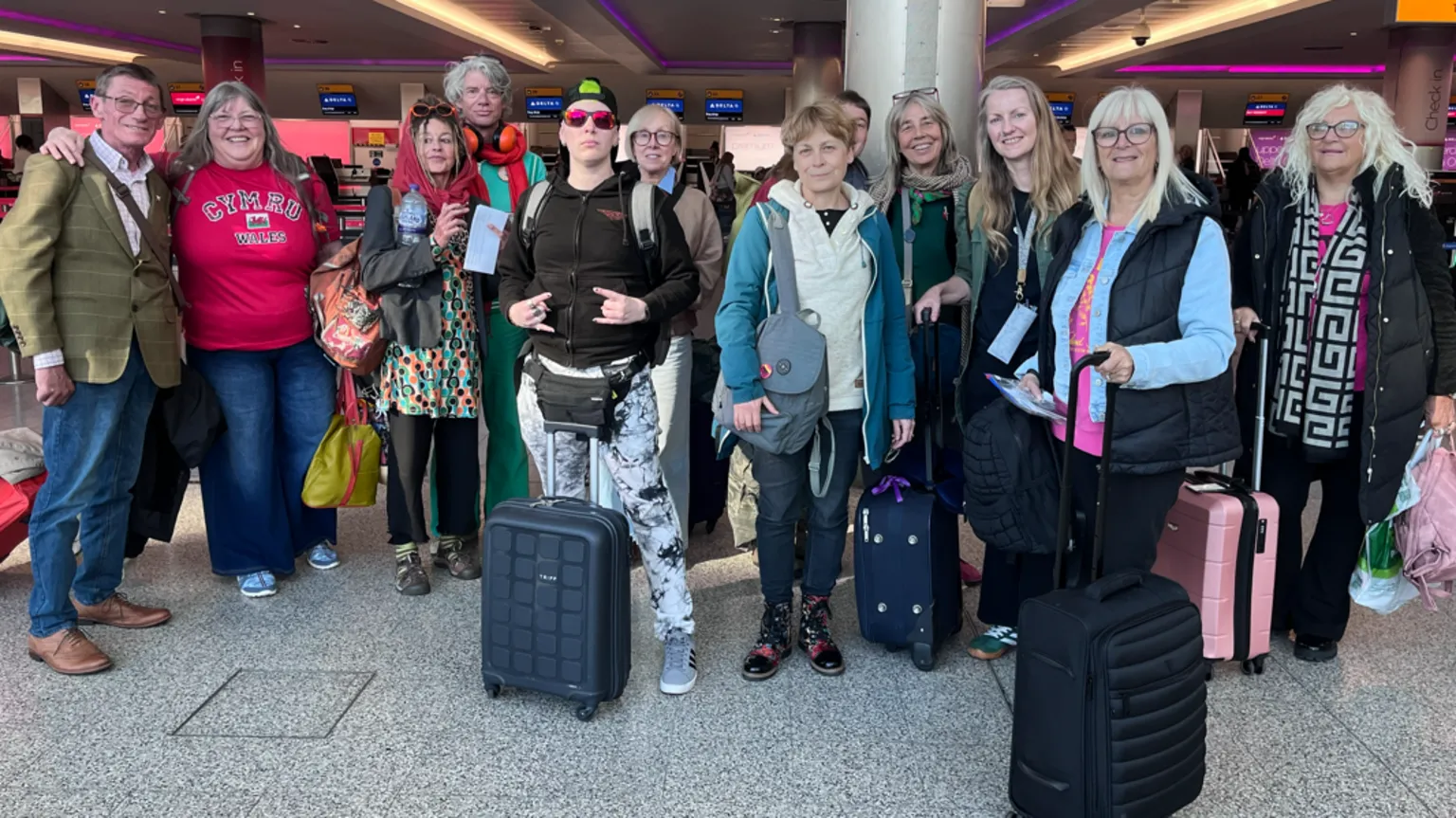 Nan Davies / Laura Robinson / BBC A large group of people stood in an airport. They have various bags and suitcases and are all smiling and looking at the camera