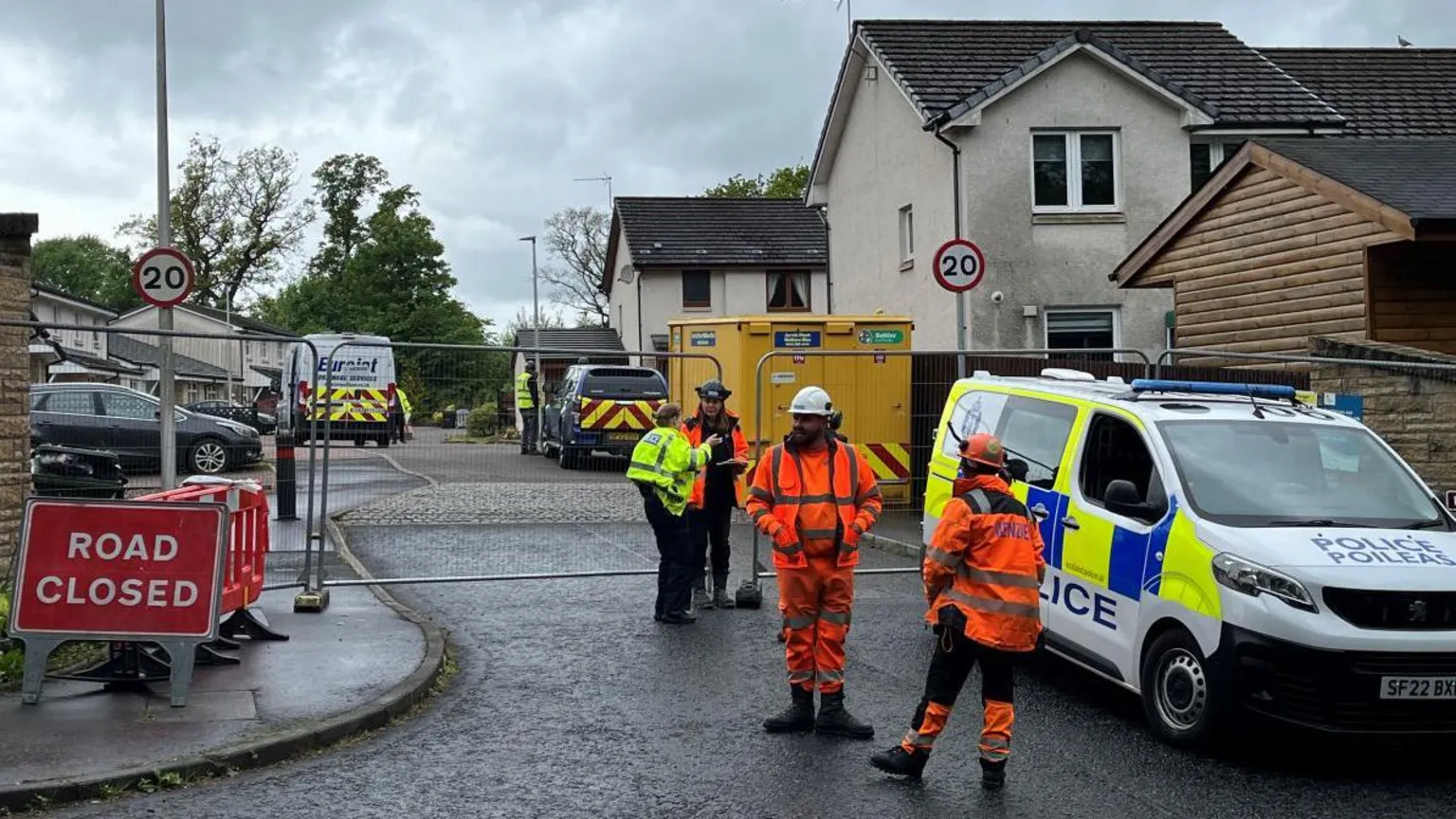 Police officers and workers wearing hi-vis stand outside a blocked-off road
