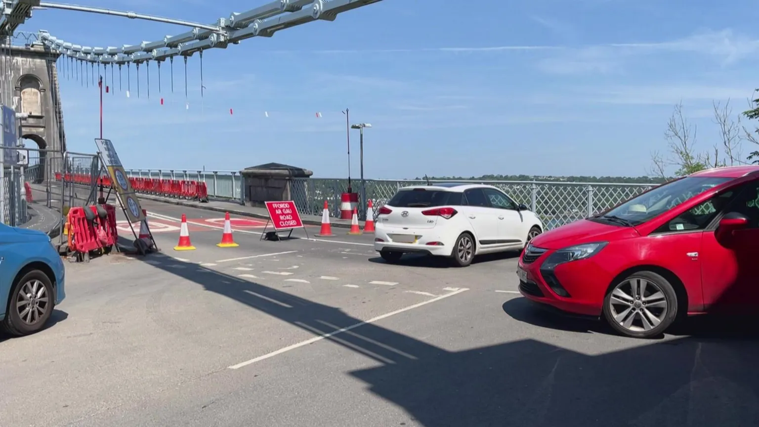 Cars turning back and reversing as orange traffic cones and a red road closure sign shuts the bridge off.