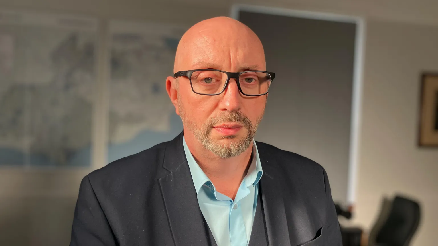 David Hinton in a light blue shirt and dark jacket. he is looking at the camera and has a stern expression.