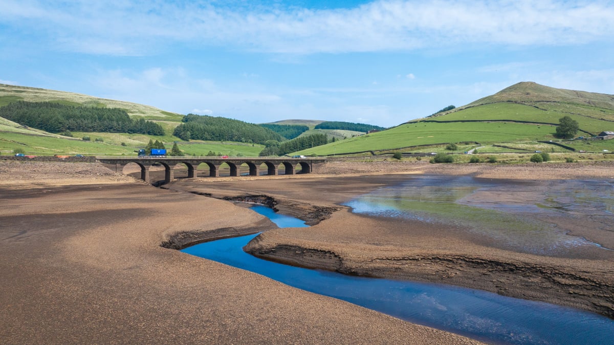 A reservoir reduced to a small channel of water with a bridge and hills in the background