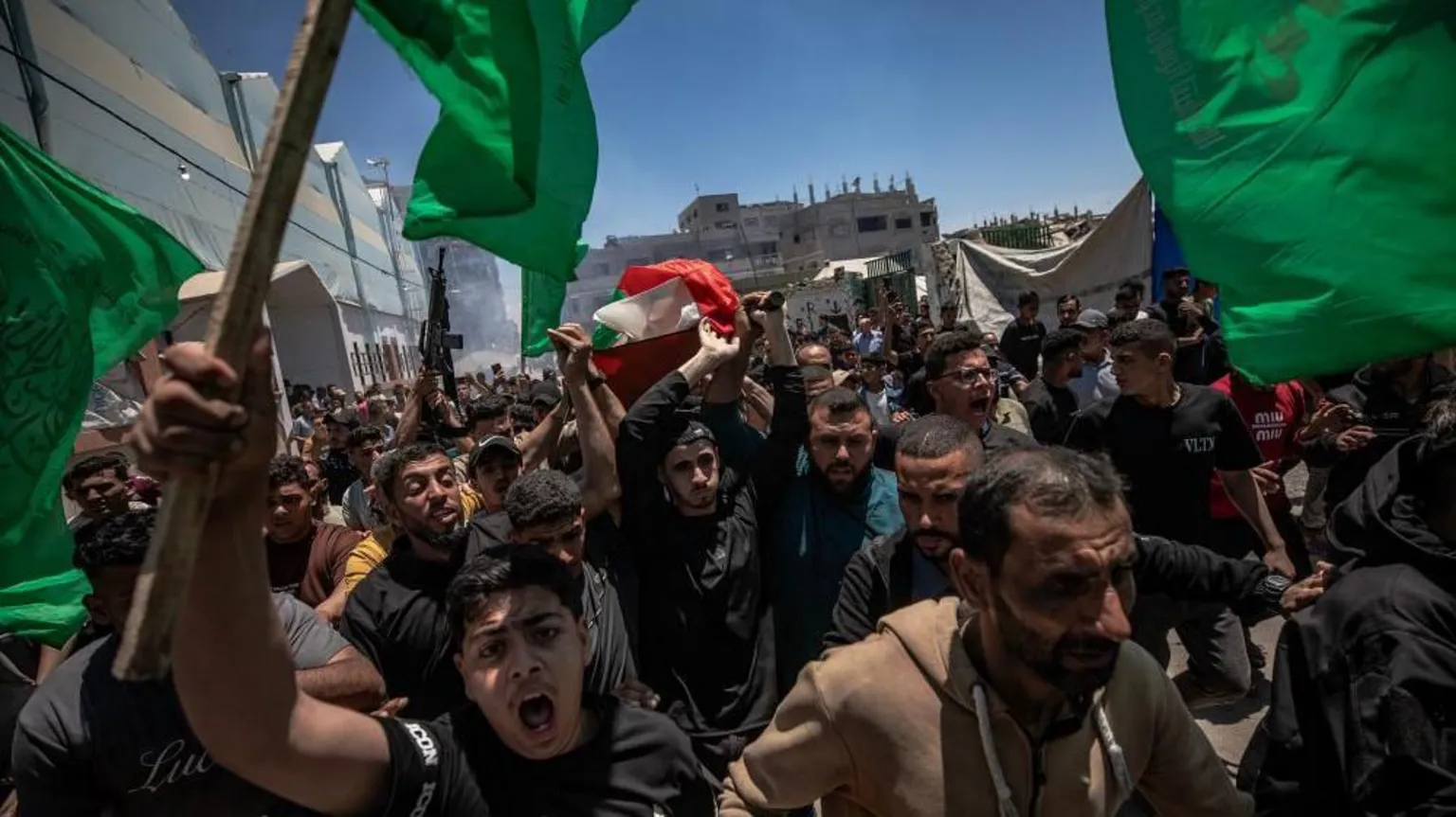 EPA/Shutterstock Dozens of people taking part in a funeral procession through Gaza City, some waving green flags and one holding a gun aloft