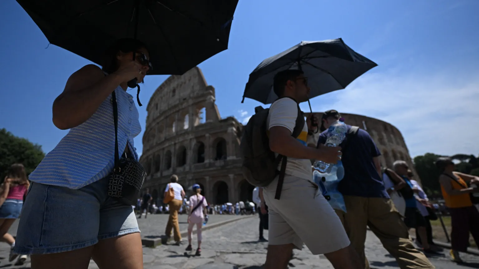 People shield themselves from the sun with umbrellas near the Colosseum in Rome
