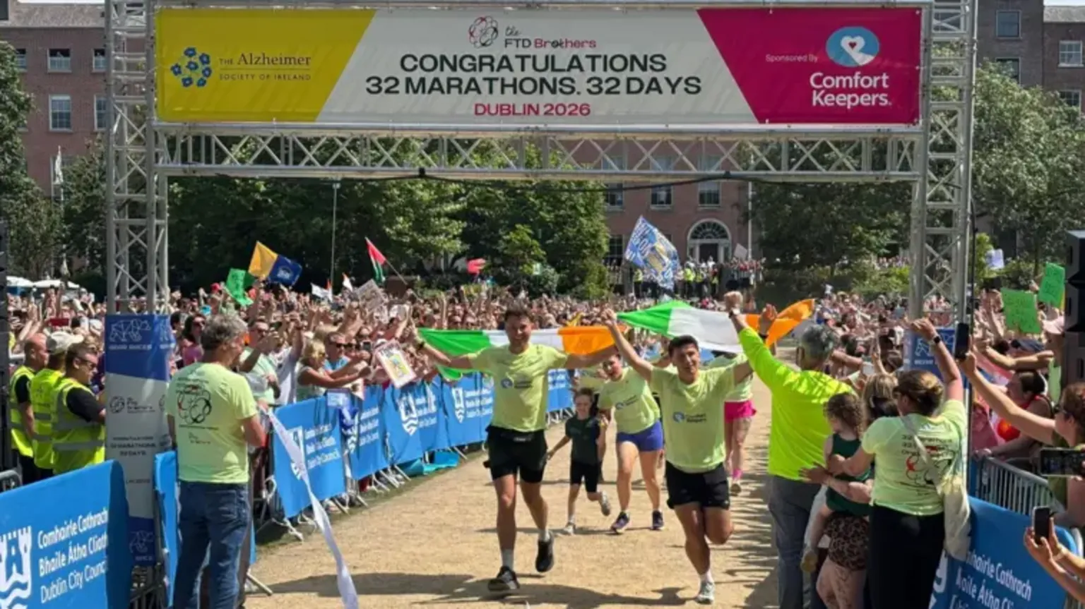 Jordan and Cian Adams crossing the finish line. They are both waving Irish flags. Above them is a banner saying 
