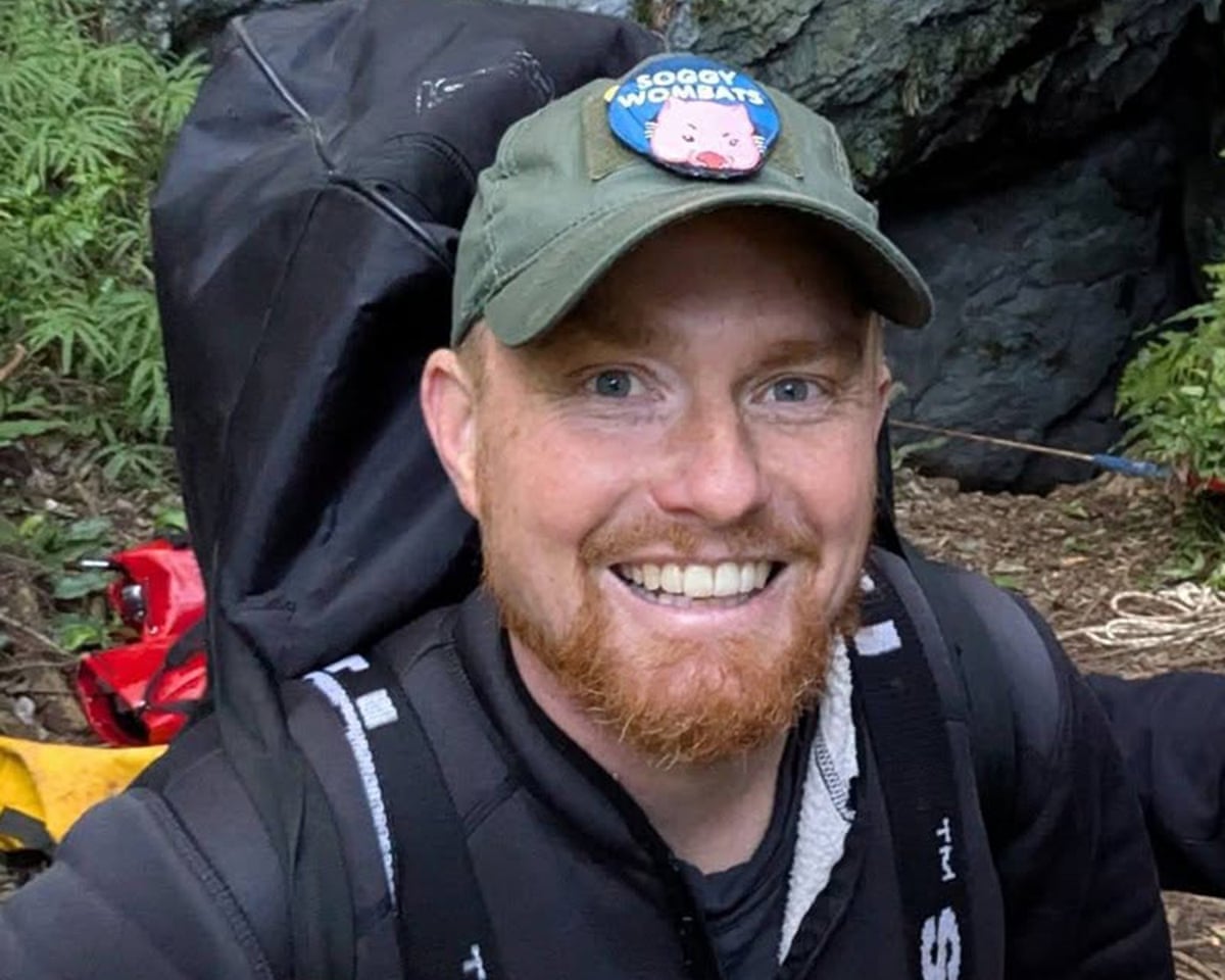 Man with a ginger beard, wearing a backpack, smiles at the camera