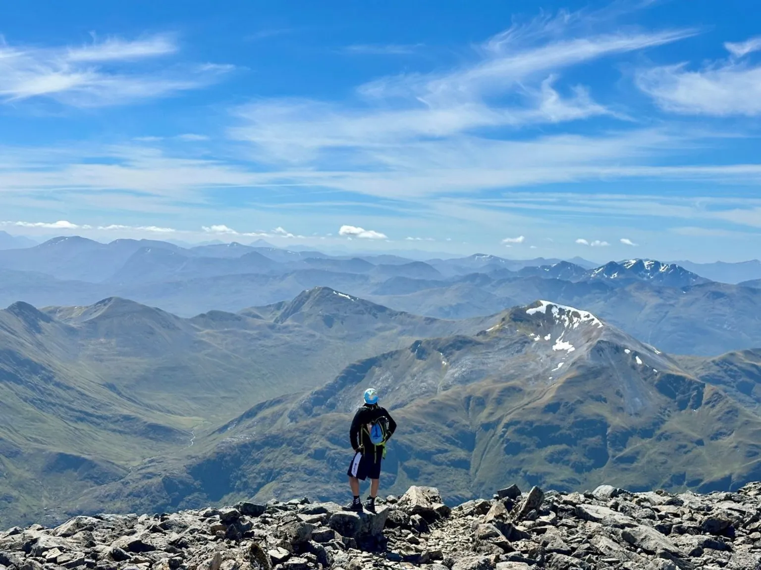 Evie McMillan A man stands at the summit of Ben Nevis with a dramatic view of adjoining hills