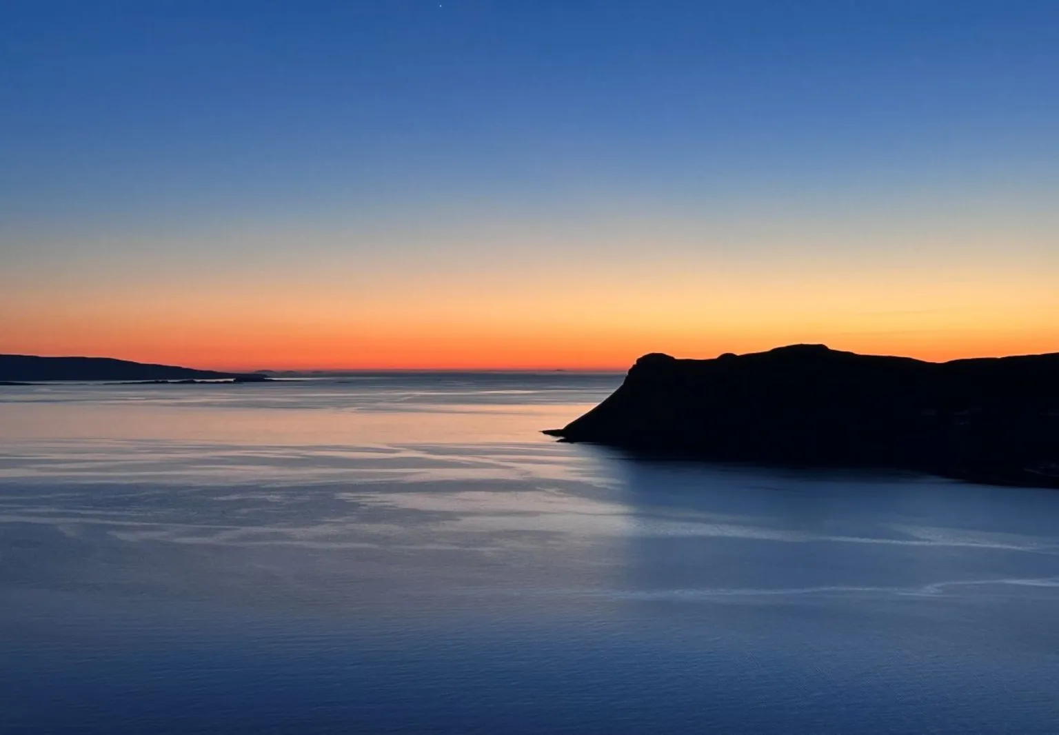 Kate Masson A sunset with a body of water in the foreground and a hill to the right of the photo