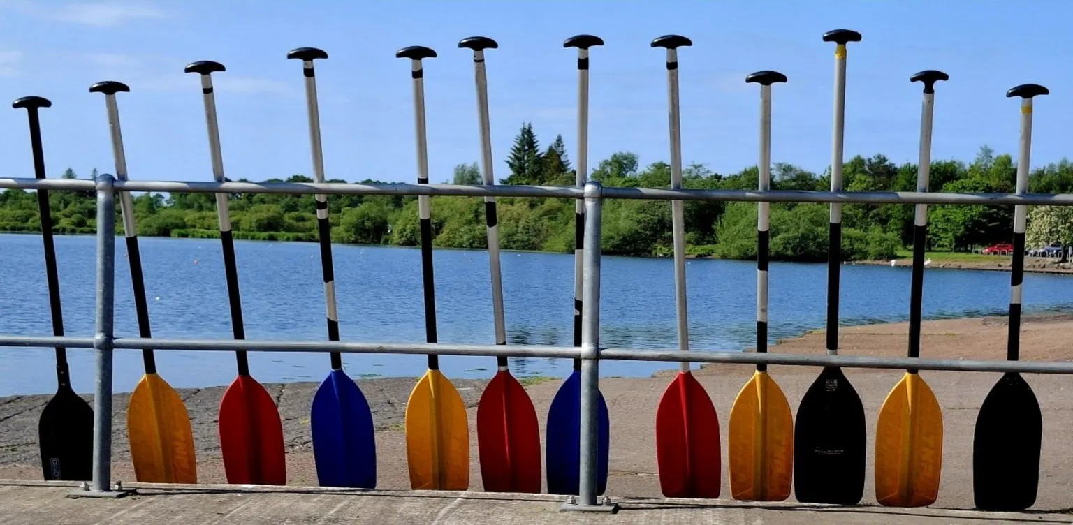 Billy Darroch A row of paddles lined up against a fence with a lake in the background
