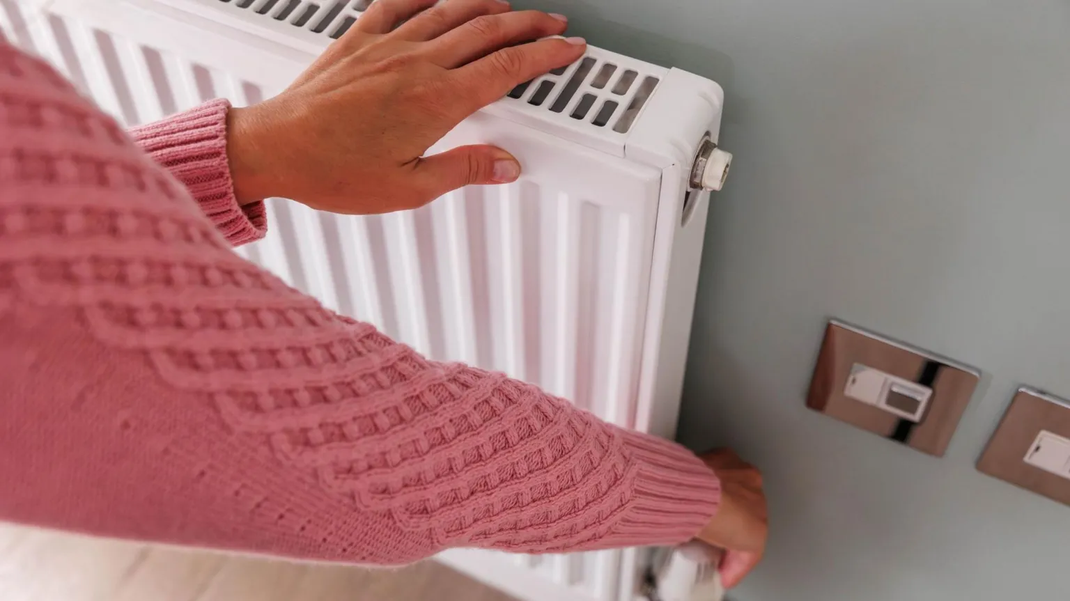 Woman's hands adjusting a heating temperature on a radiator at home