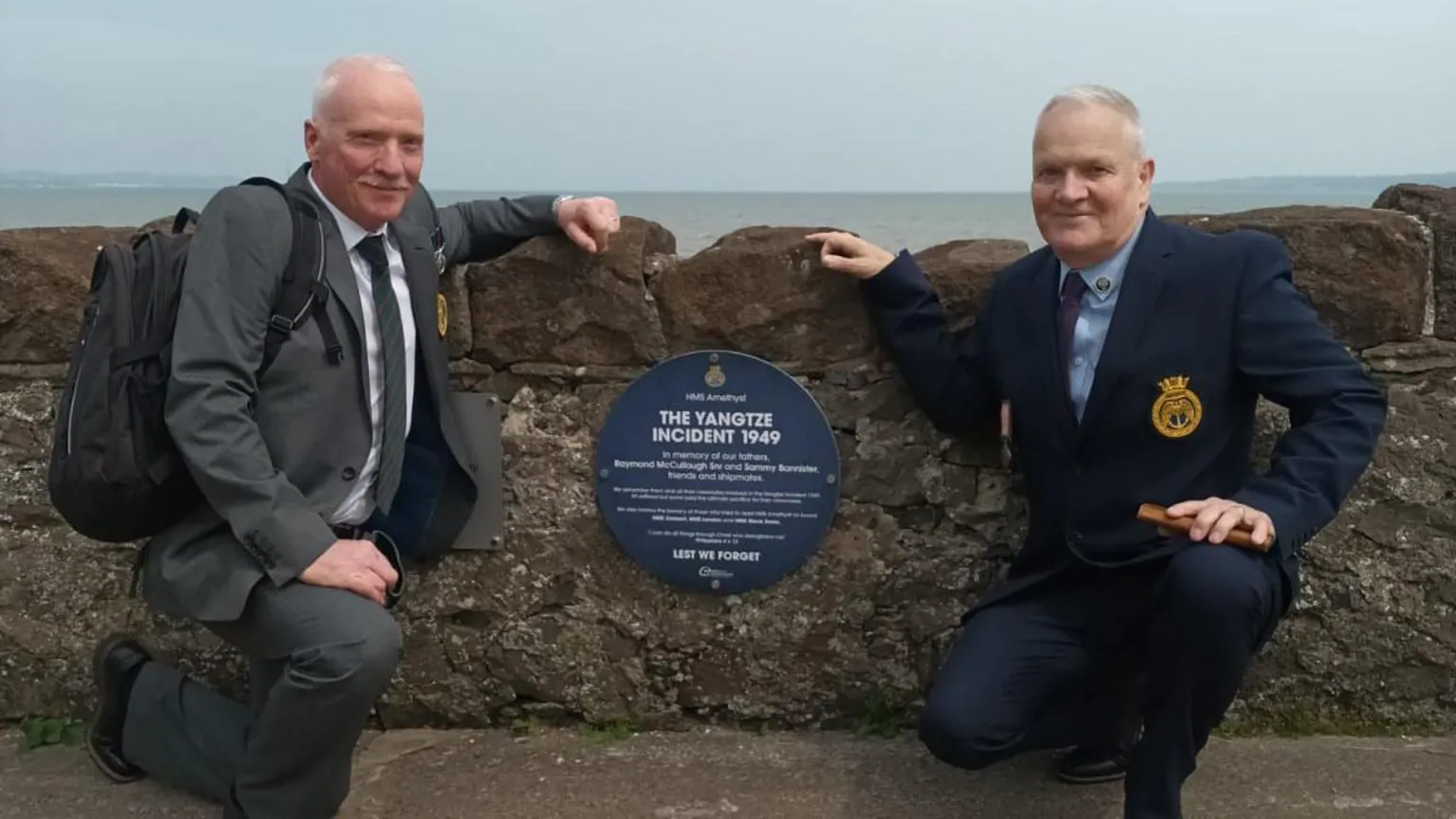 Andrew Bannister Two men in suits kneeling down next to a blue circle plaque on the wall on the coast line. The plaque is remembering the 1949 Yangtze Incident.
