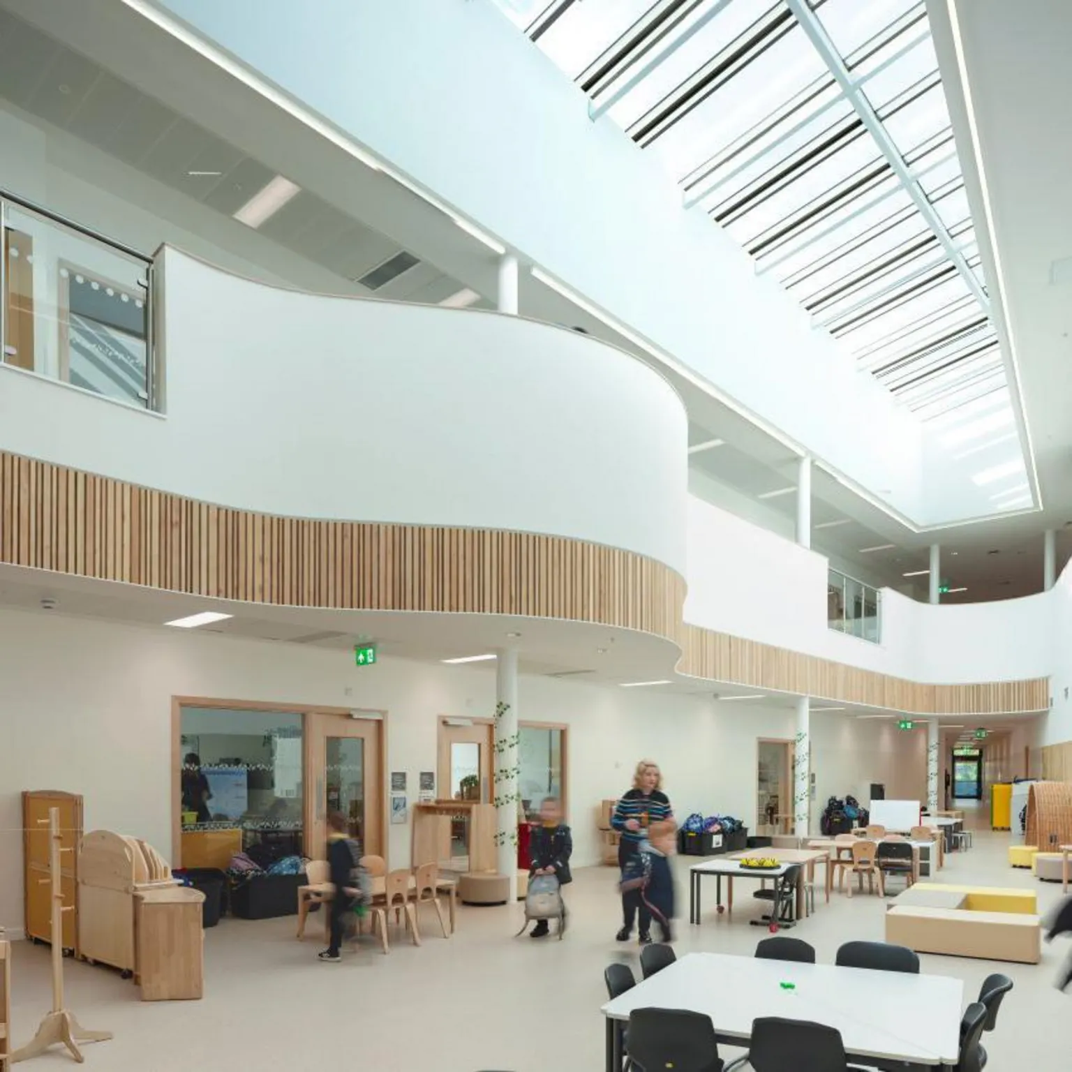 David Barbour Neilston Learning Campus, the bright interior of a building with a skylight, and adults and children inside.
