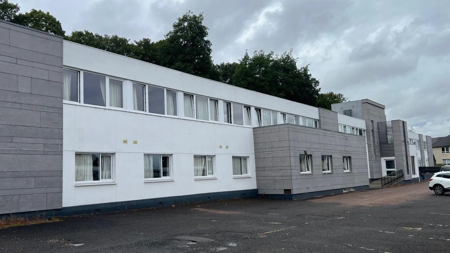 A grey and white two-storey building with a car park at the front