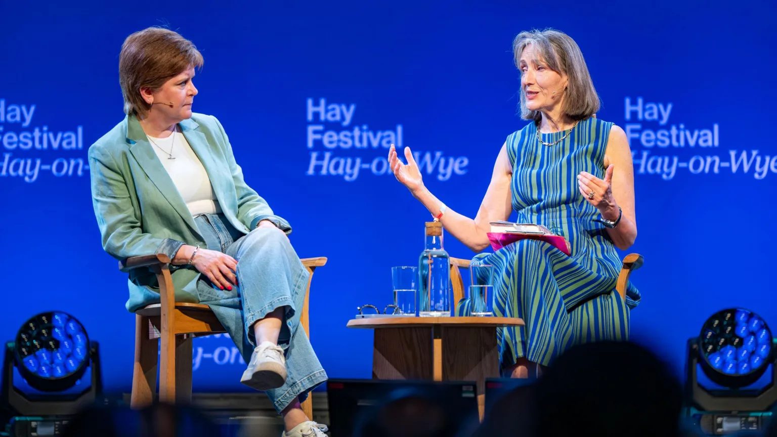  Two women in conversation while seated on a stage in front of an audience