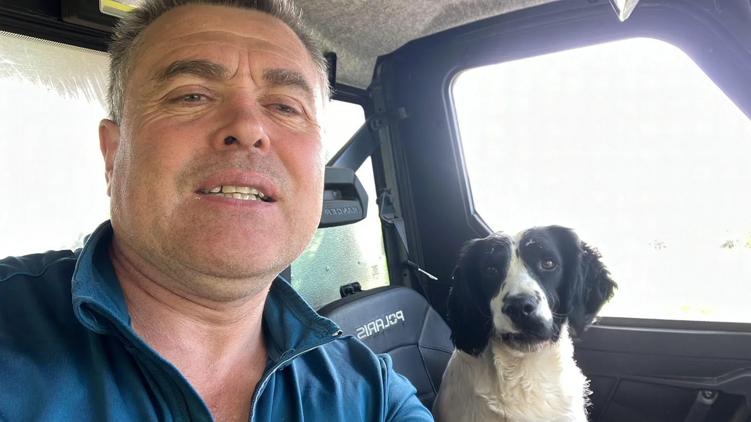 Thomas Conway A man is pictured in the front seat of a jeep, with a springer spaniel dog sitting in the passenger side seat. the man is wearing a blue jumper. the dog is black and white in colour.