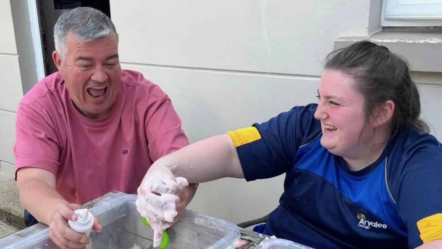 Conor and Ruby laughing. Conor has grey hair and is wearing a red t-shirt. Ruby has brown hair and is wearing a blue t-shirt.