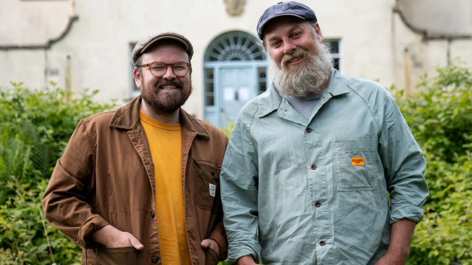 Shelley Richmond/Hello Halo/BBC Scotland Banjo Beale - a man with glasses, a flat cap and a beard, wearing a brown jacket and orange shirt and Ro Christopher, a man in a aquamarine shirt, with a white beard and a flat cap.