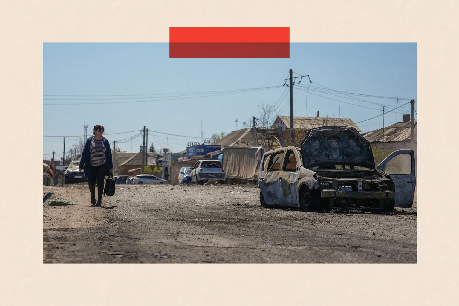 Global Images Ukraine via A woman walks along a street in the sunshine, carrying a shopping bag, next to a bombed-out car