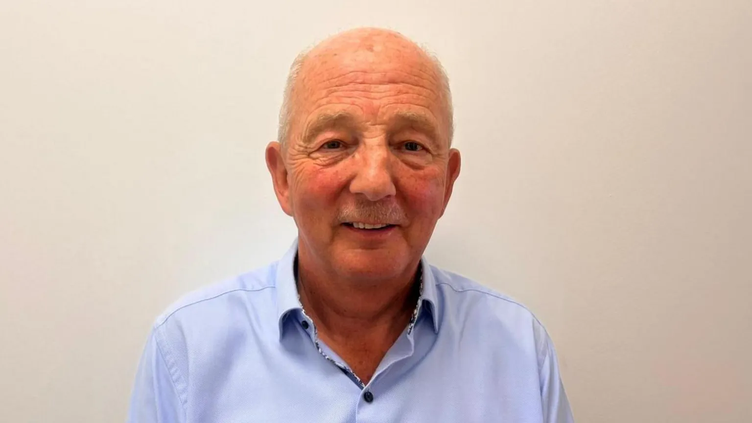 Robert Gordon is wearing a light blue shirt. He is smiling and standing in front of a plain background. 