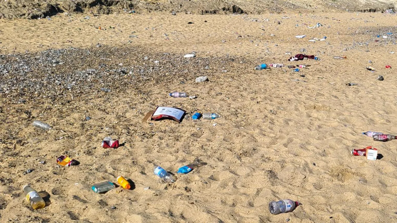 Serco/NNDC Litter including cans, cardboard packaging and bottles discarded on a sandy beach on a sunny day. 