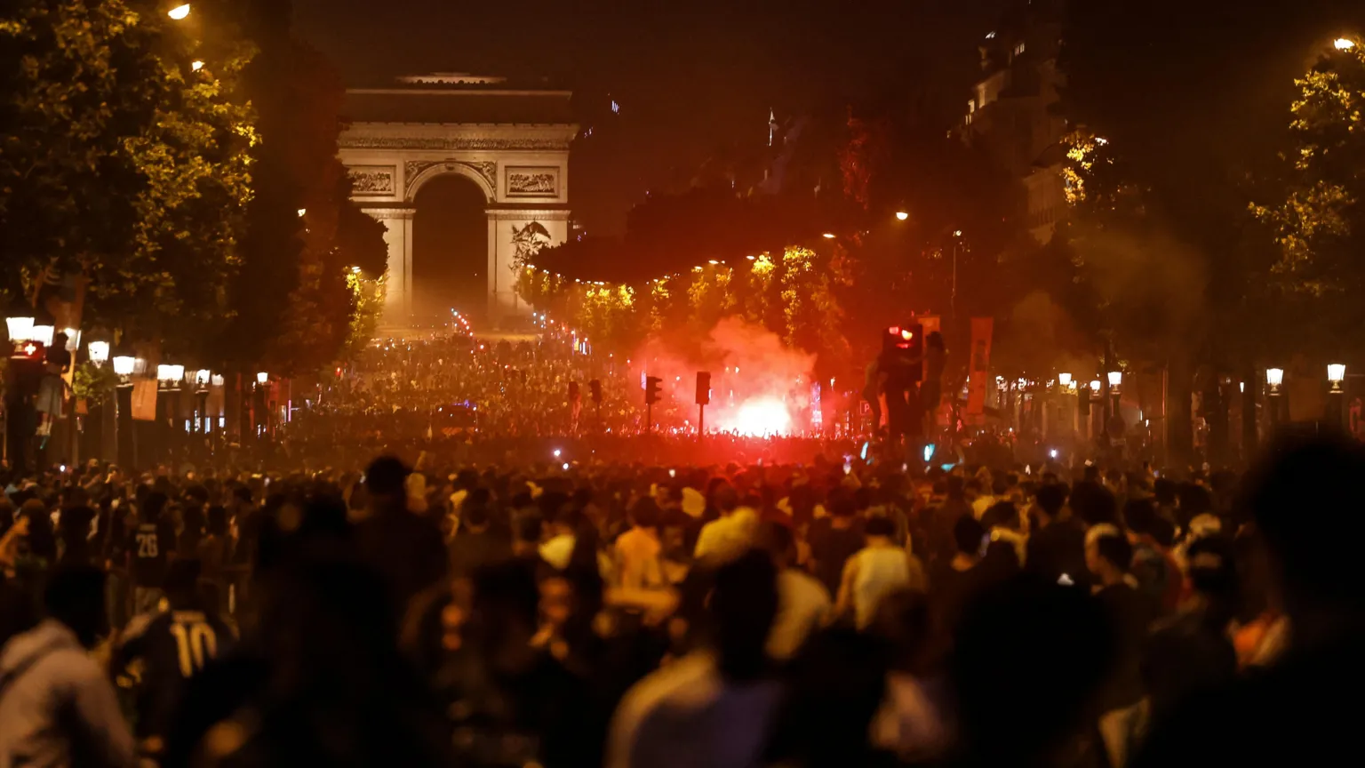 AFP via Bustling crowds swamp Avenue des Champs-Élysées, lit up by a ball of red flares along the landmark mall. The Arc de Triomphe can be seen at the end of the avenue.