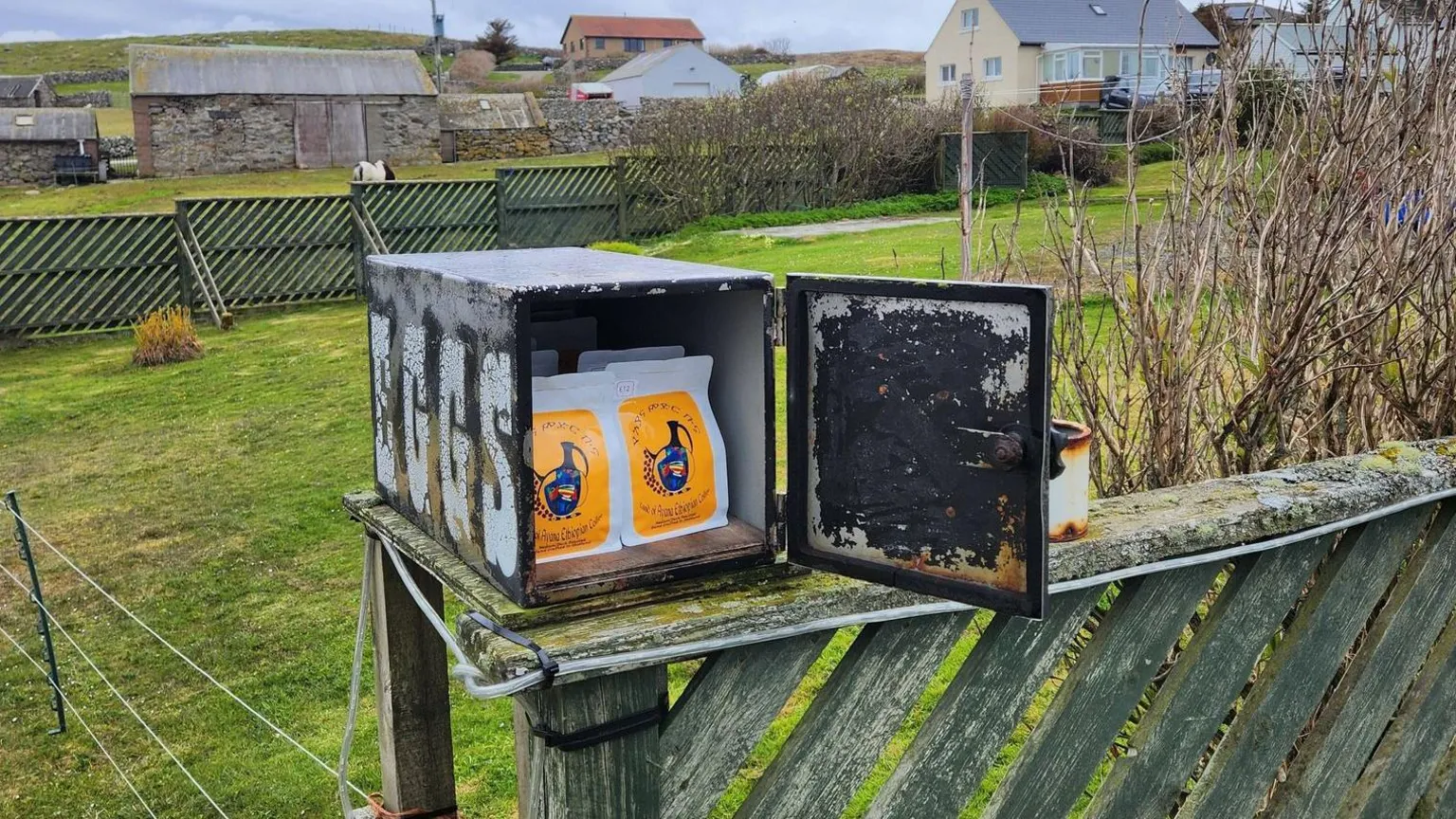 Netsanet Sori A black box placed on a green fence, containing colourful bags of coffee beans.