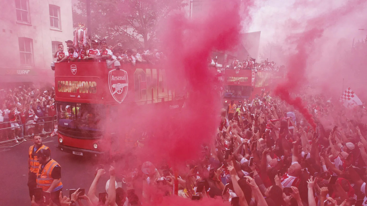 EPA Crowds cheering on the side of a street one of the celebratory open top buses is going through, holding up flares blowing out red smoke