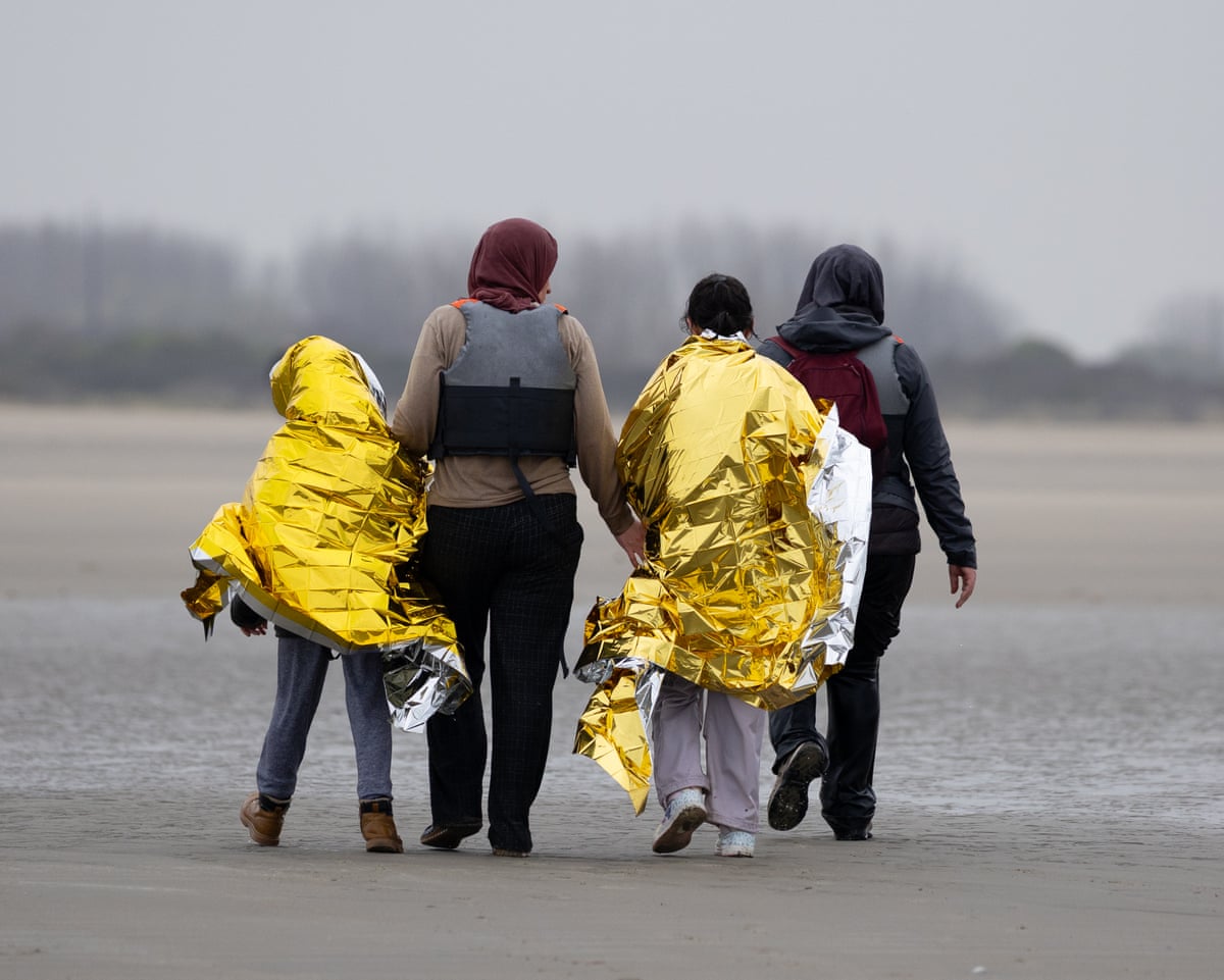 Two women walk away from the camera, accompanying two children wrapped in gold foil blankets