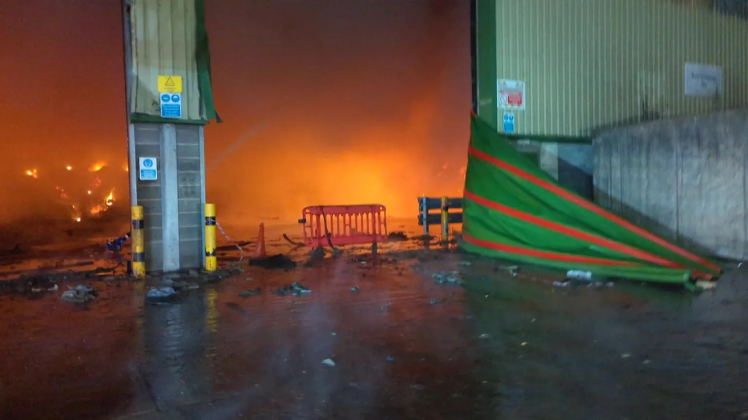 Nottinghamshire Fire and Rescue Service A fire inside a recycling centre in Nottinghamshire. The centre is filled with smoke, meaning the fire is the only thing that can be seen inside. Outside of the centre, the floor is wet and covered with black debris.