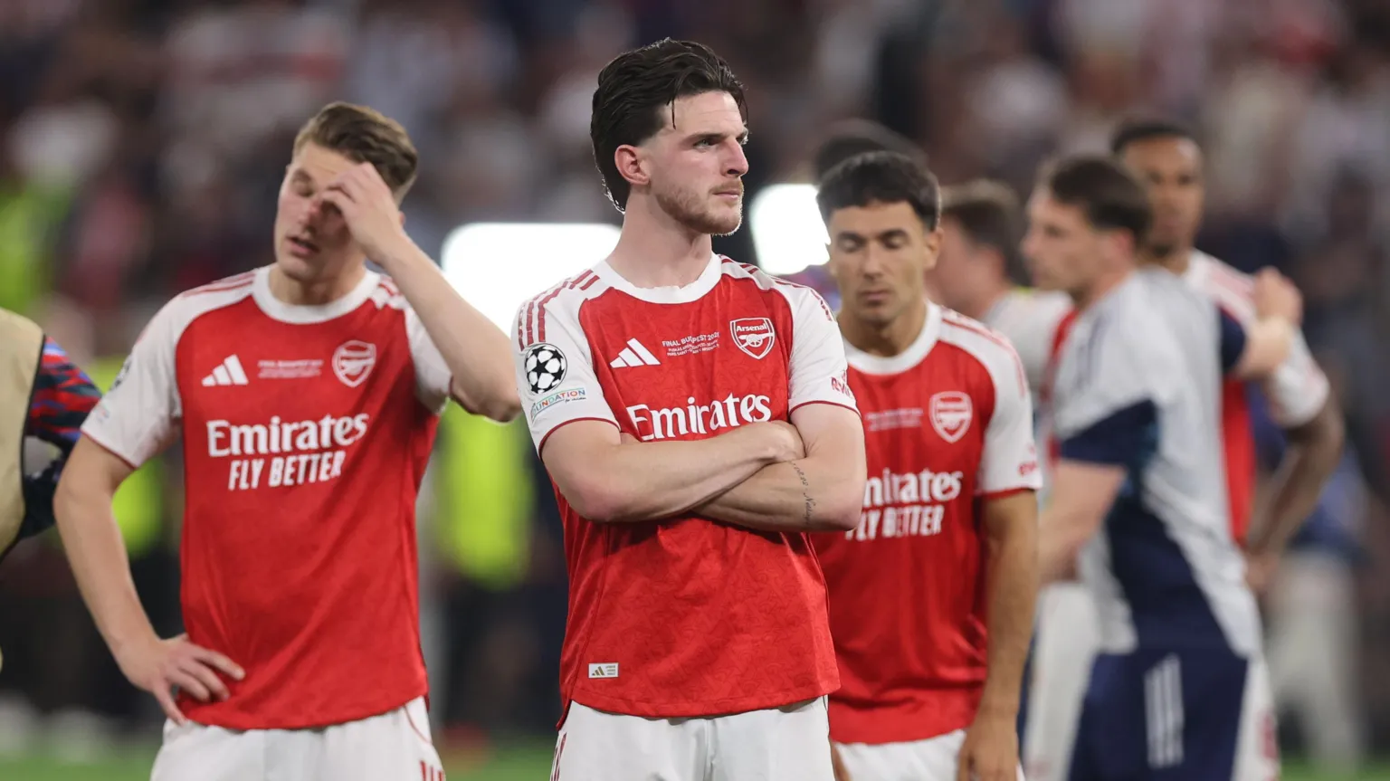  Declan Rice wearing a red Arsenal kit while standing on a pitch with his arms crossed. 