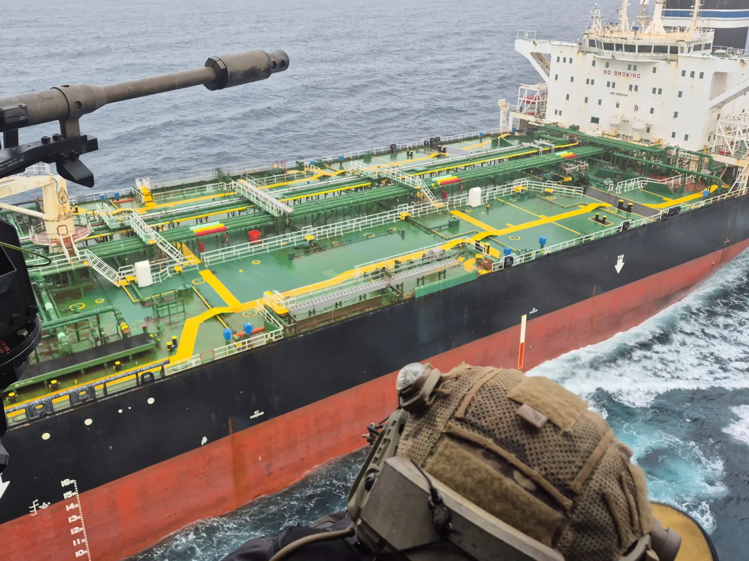  An image from on board a French navy helicopter as it approaches an oil tanker said to be part of Russia's shadow fleet. A navy officer can be seen wearing a camouflage military helmet. 