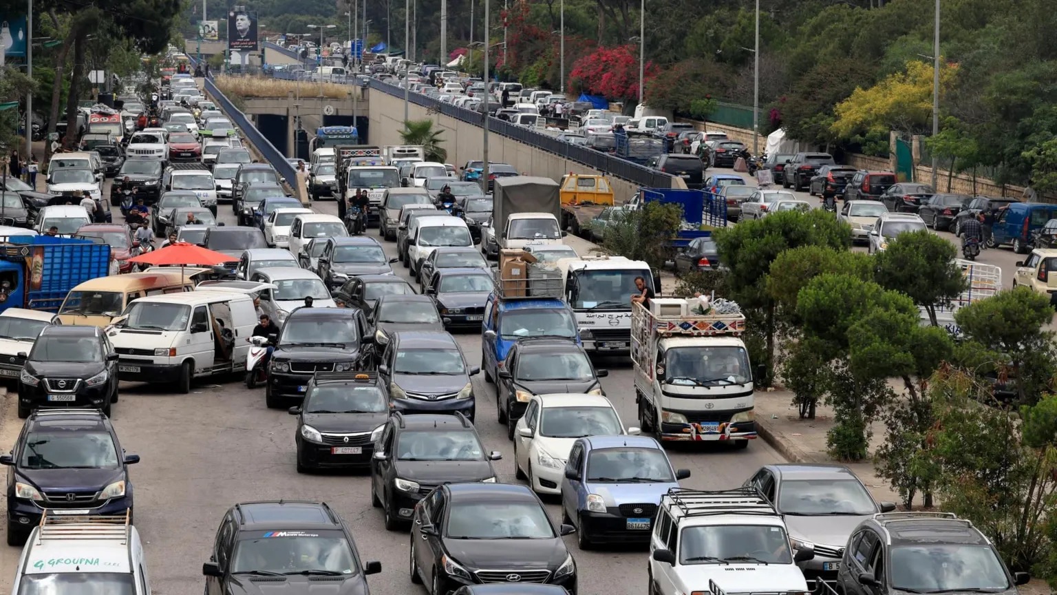  Traffic jam on a main road in Beirut's southern suburbs, with up to five cars across at one point just as vehicles on a road are joined by those emerging from a tunnel. There are some trees dividing the road, with cars as far as the eye can see on the other side, too.
