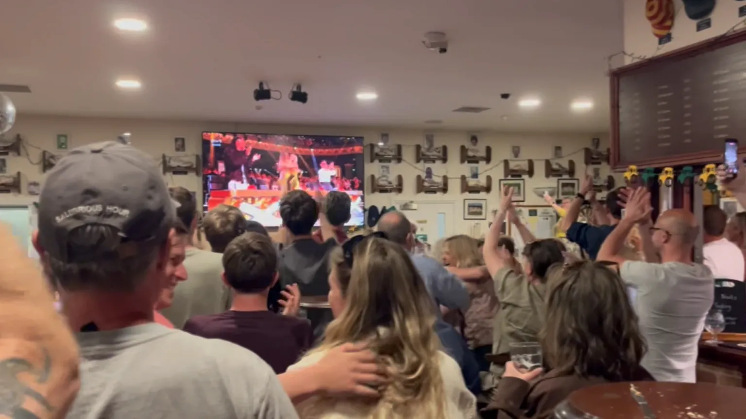 Oxford Downs Cricket Club A view of supporters cheering the choir's winning moment at the Oxford Downs Cricket Club. They are clapping and recording the TV's broadcast.