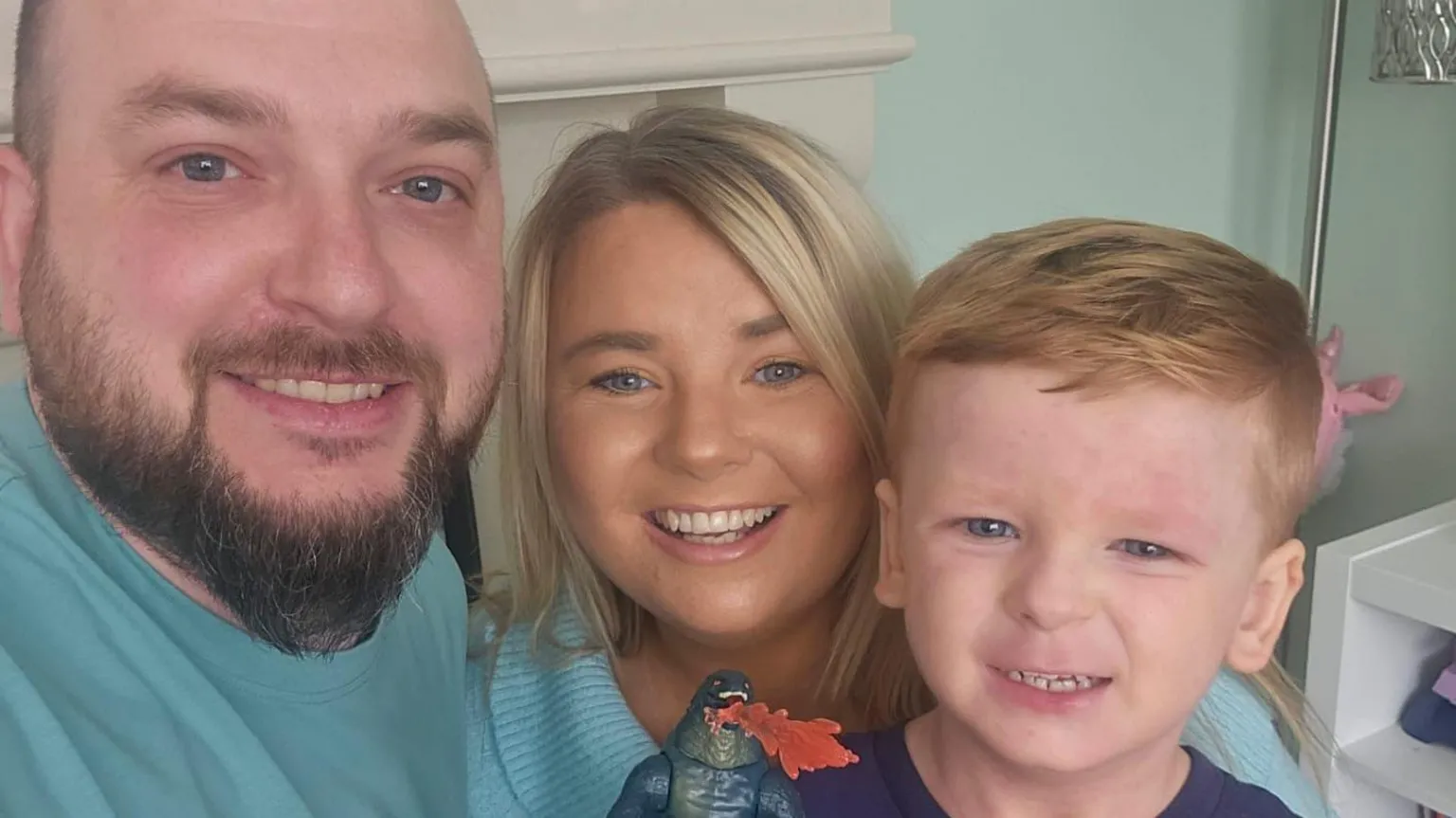 Family Handout A man with a bald head and a beard wearing a green tee shirt smiles at the camera (left) (Middle) A woman with blonde hair, wearing a green sweatshirt smiles at the camera (Left) A boy with red hair smiles at the camera, he is wearing a blue top and is holding an action figure up to the camera.