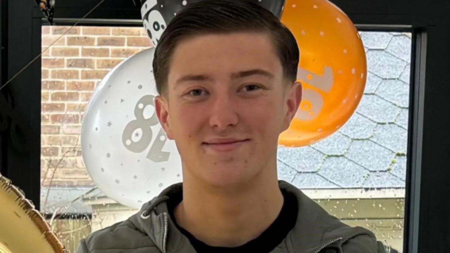 Police handout An 18-year-old man standing in front of orange, white and black balloons by a window. He has short dark hair and is smiling and is wearing a blue jacket and a black top underneath.